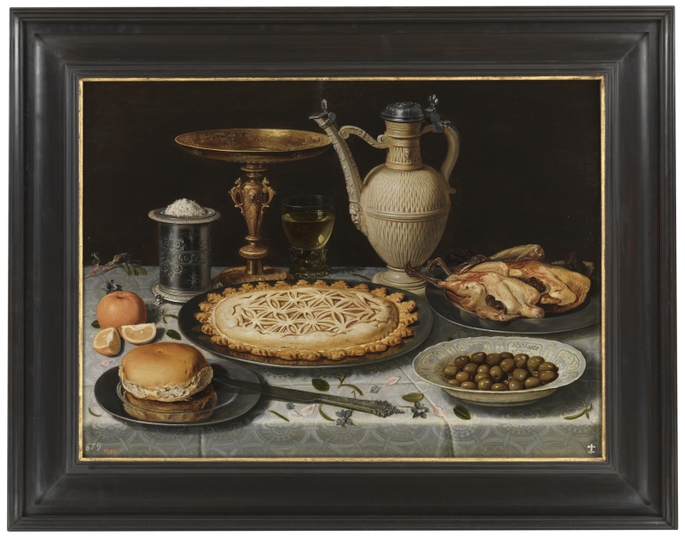 Mesa con mantel, salero, taza dorada, pastel, jarra, plato de porcelana con aceitunas y aves asadas